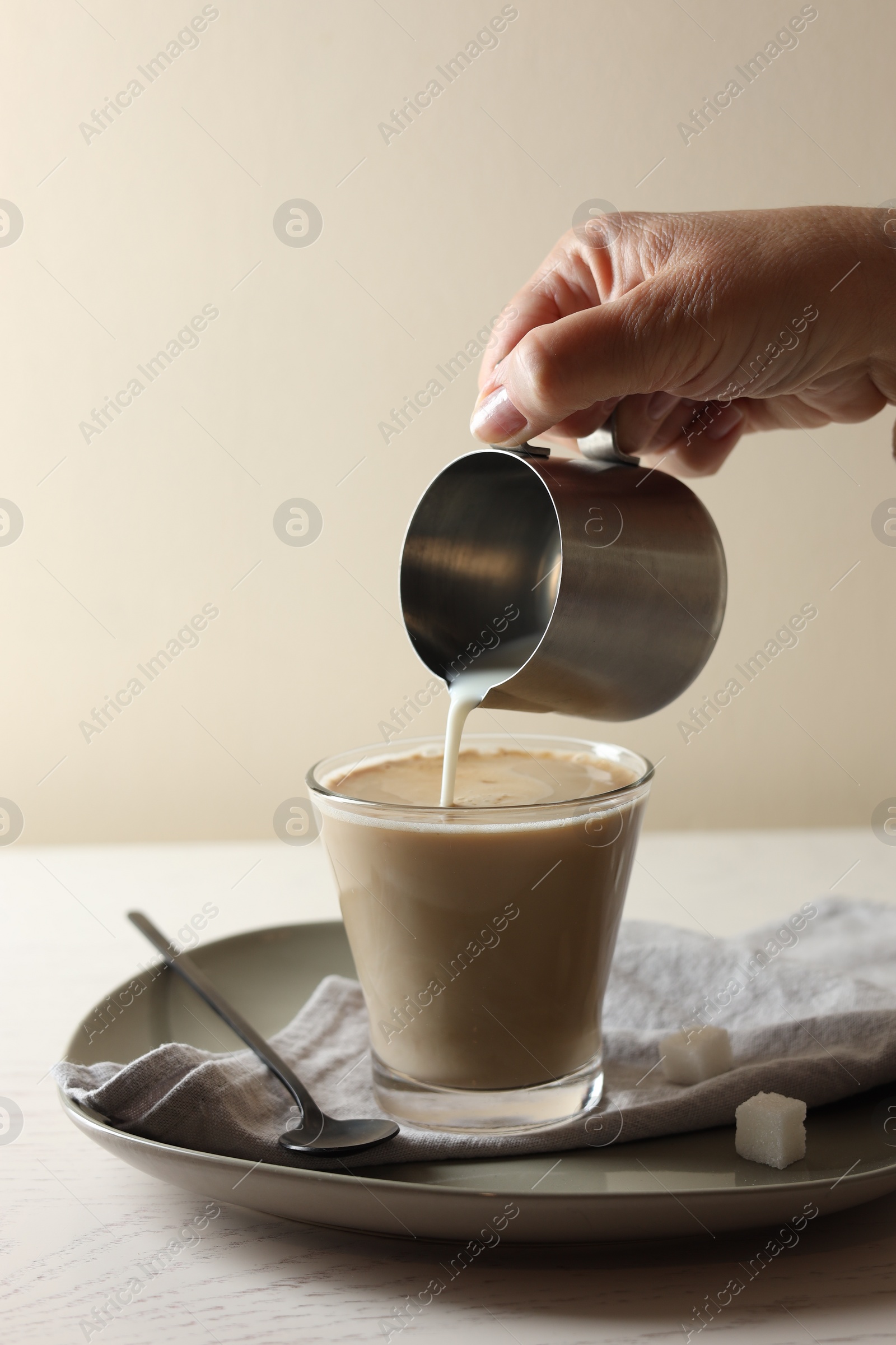 Photo of Pouring milk into cup with coffee on white wooden table, closeup