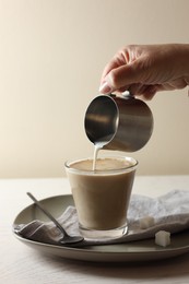 Photo of Pouring milk into cup with coffee on white wooden table, closeup