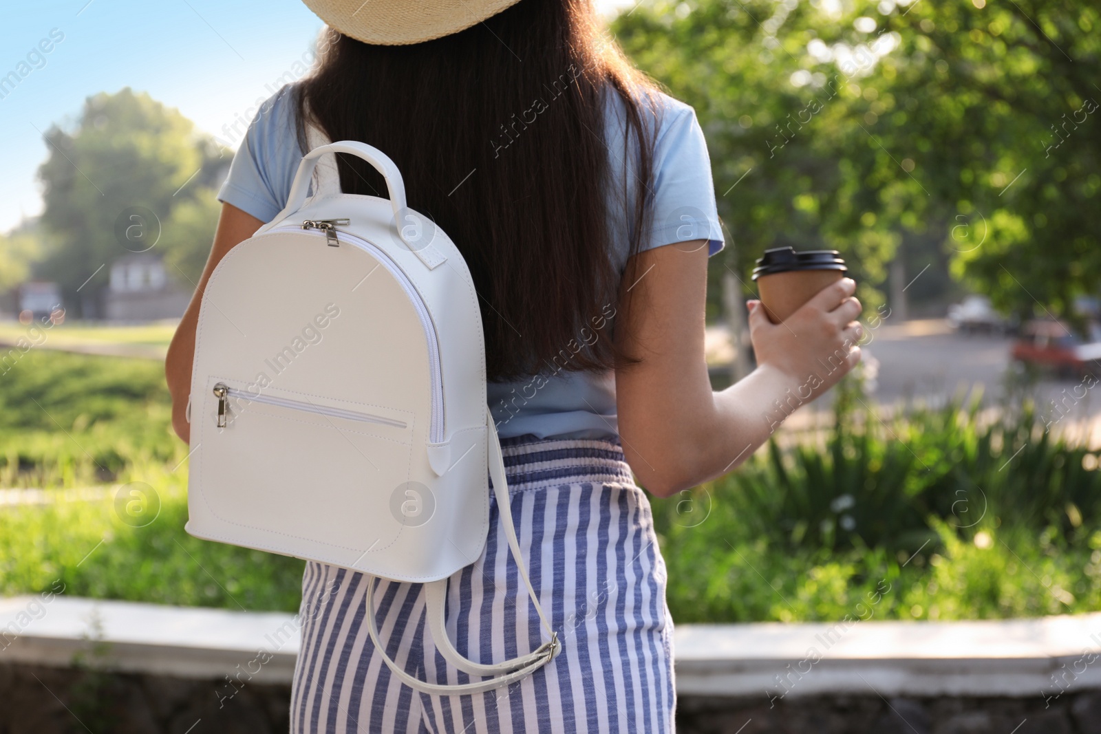 Photo of Young woman with stylish backpack and cup of coffee in city park, back view