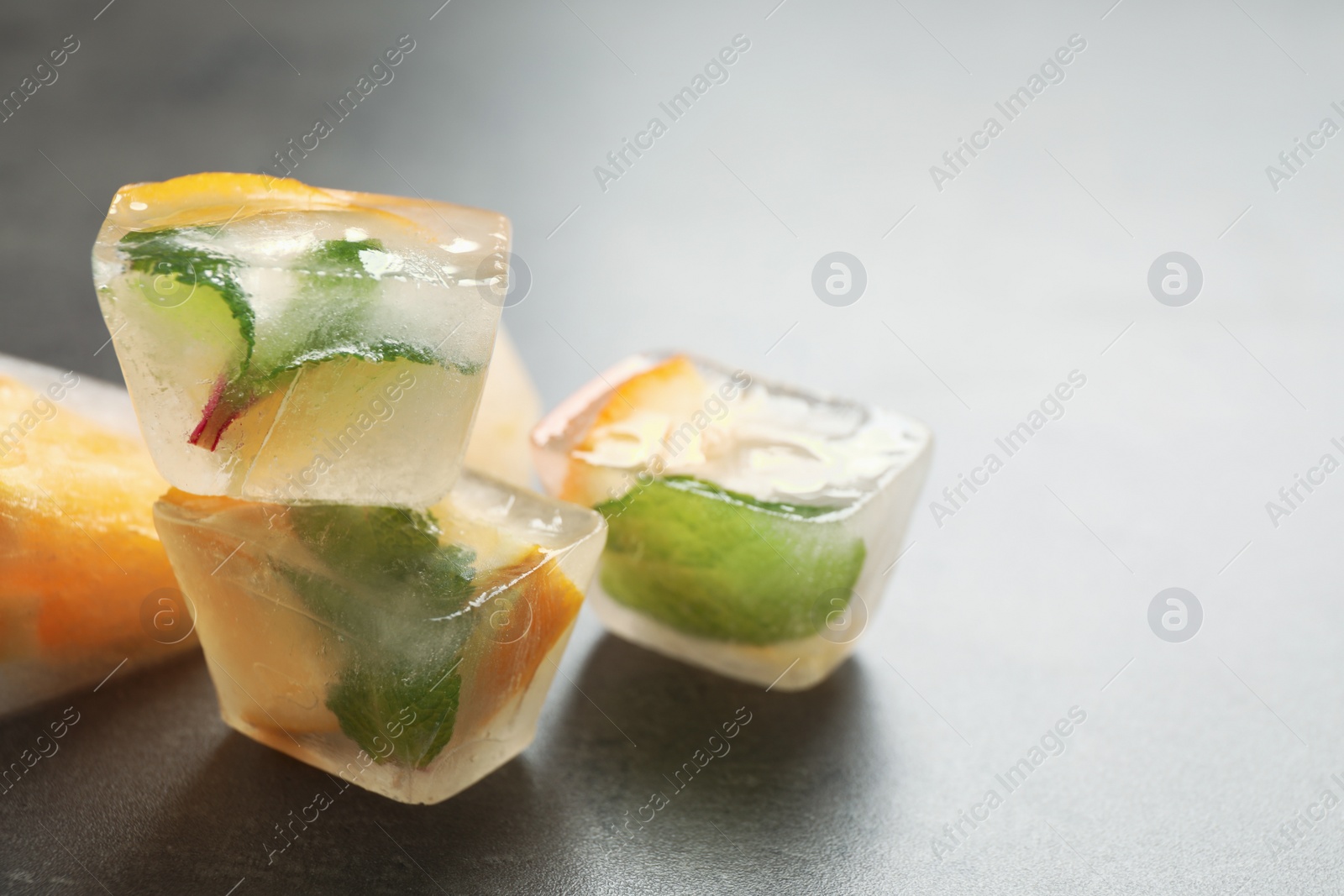 Photo of Ice cubes with orange and mint on grey table, closeup. Space for text