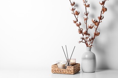 Burning candles in wicker basket and vase with cotton branches on table against white background. Space for text