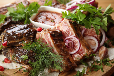 Photo of Delicious roasted ribs and liver with herbal on wooden board, closeup