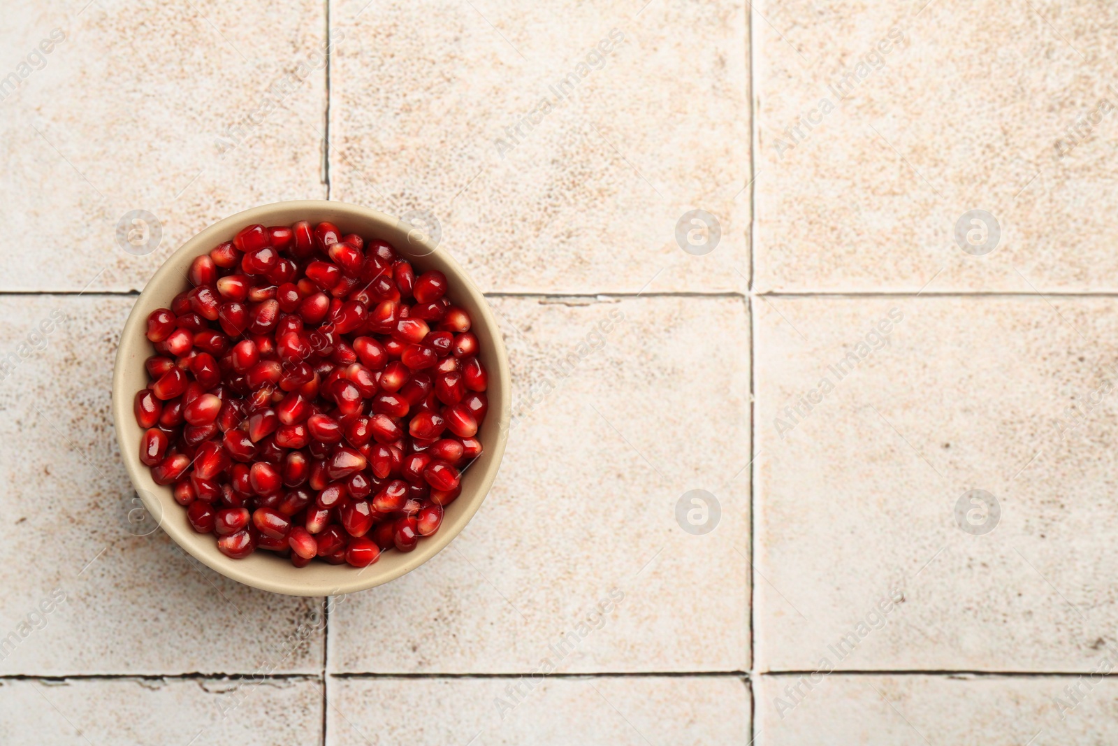 Photo of Tasty ripe pomegranate grains on tiled table, top view. Space for text