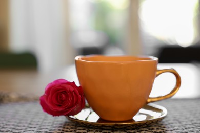 Photo of Cup of hot drink and red rose on table indoors, closeup