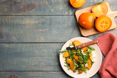 Photo of Delicious persimmon salad served on light blue wooden table, flat lay. Space for text