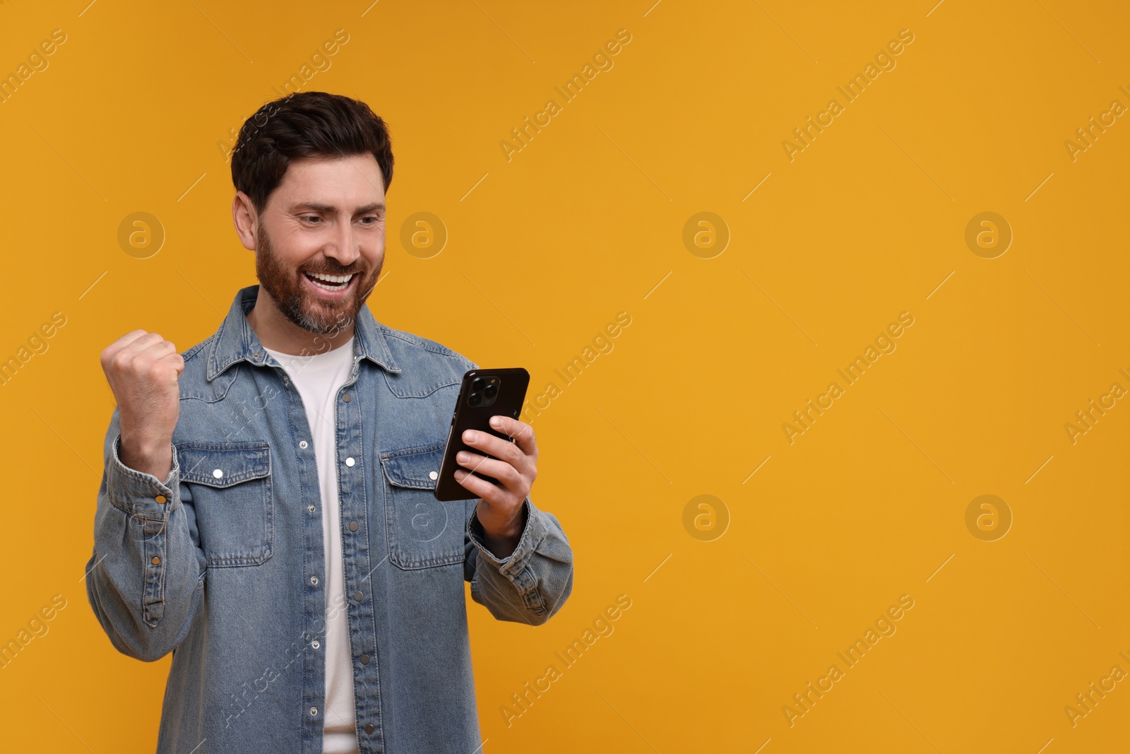 Photo of Happy man with smartphone on orange background. Space for text