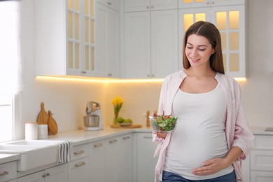 Photo of Young pregnant woman with vegetable salad in kitchen, space for text. Healthy eating