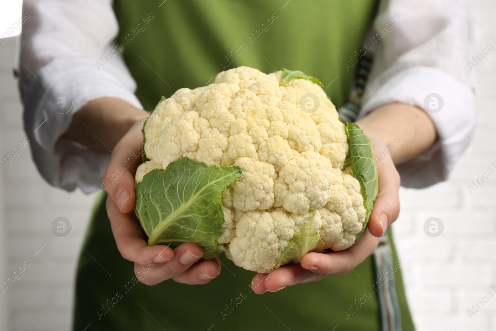 Photo of Woman holding fresh cauliflower against brick wall, closeup