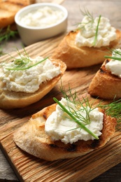 Photo of Toasted bread with tasty cream cheese on wooden board