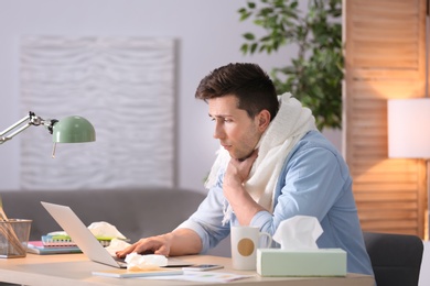 Photo of Sad exhausted man suffering from cold while working with laptop at table