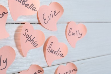 Photo of Paper stickers with different names on white wooden table, closeup. Choosing baby's name