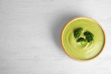 Delicious broccoli cream soup served on white wooden table, top view. Space for text