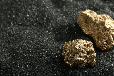 Photo of Shiny gold nuggets on black sand, closeup. Space for text