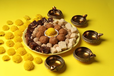 Happy Diwali. Composition with diya lamps, chrysanthemum flowers and delicious Indian sweets on yellow table