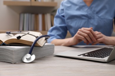 Photo of Woman with book, stethoscope and laptop at table indoors, closeup. Medical education