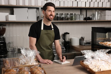 Photo of Happy seller writing something at cashier desk in bakery shop