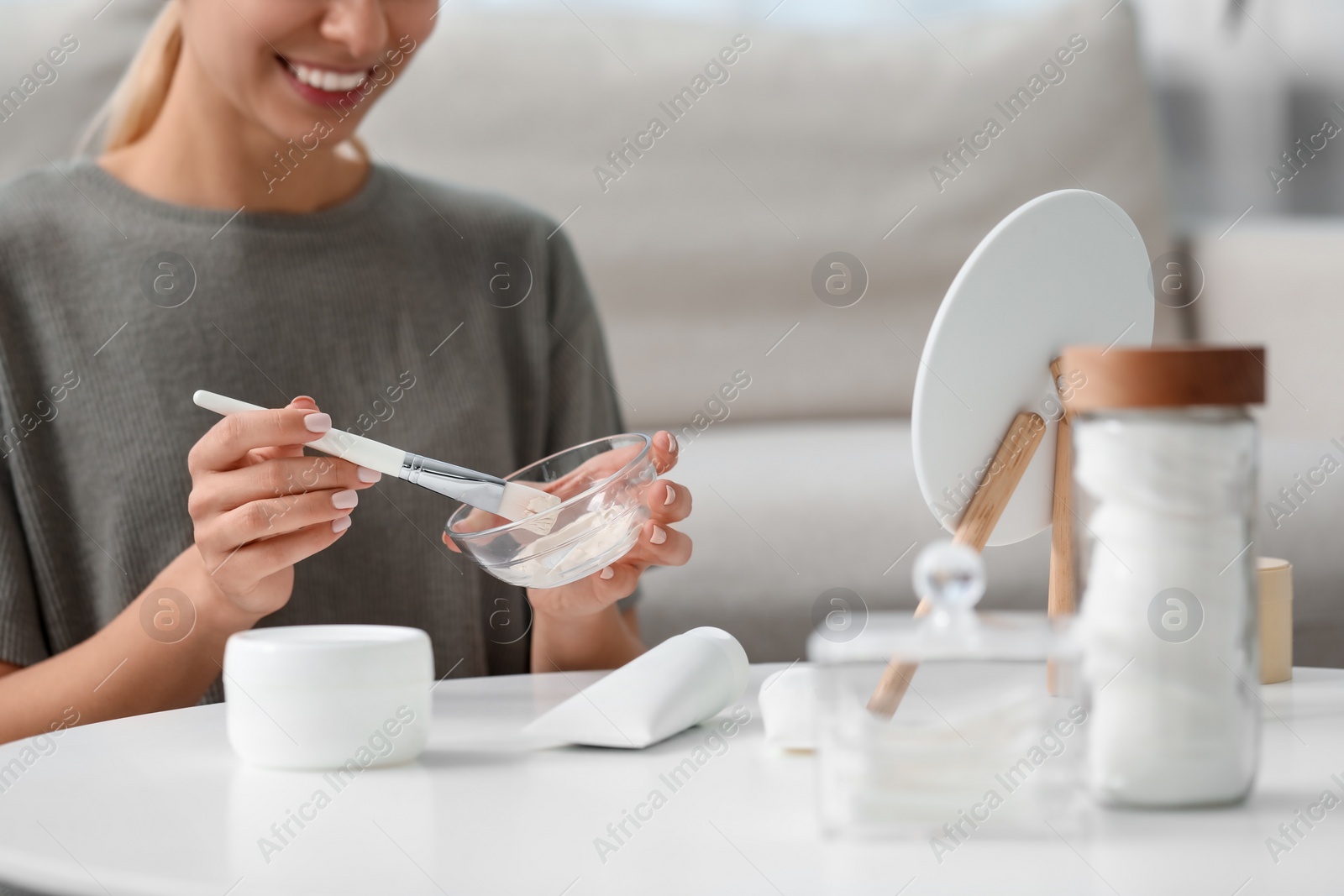 Photo of Young woman preparing face mask in front of mirror at home, closeup. Spa treatments