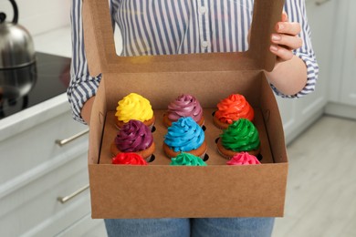 Woman holding box with delicious colorful cupcakes indoors, closeup