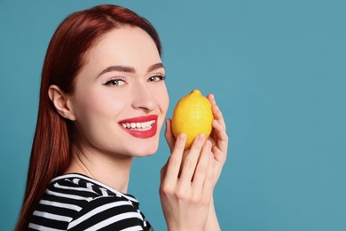 Photo of Happy woman with red dyed hair holding whole lemon on light blue background, space for text