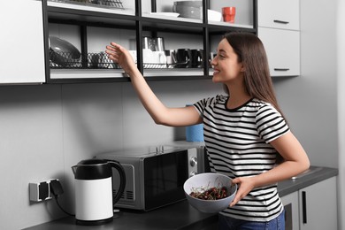 Happy young woman with bowl of cherries in hostel kitchen