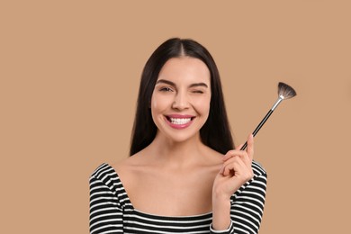 Photo of Happy woman with makeup brush on light brown background