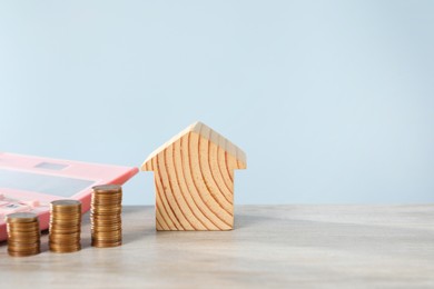 Photo of House model, calculator and coins on wooden table against light blue background, space for text