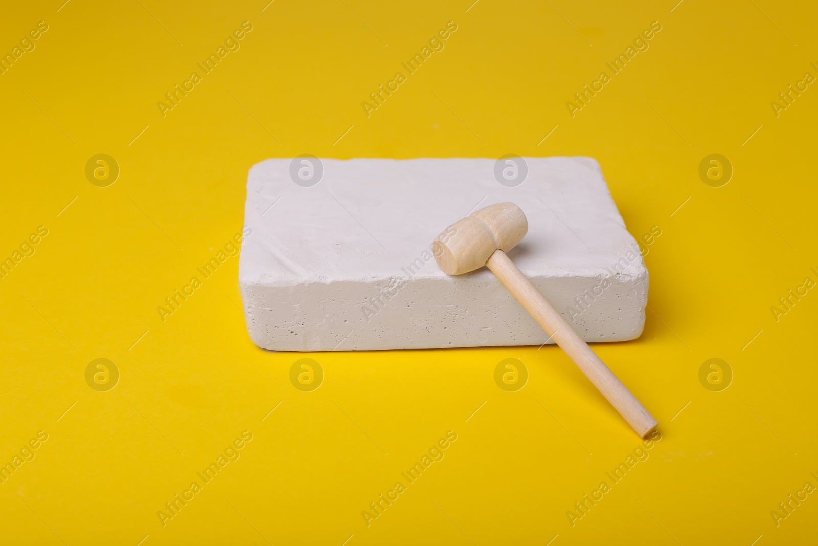 Photo of Educational toy for motor skills development. Excavation kit (plaster and wooden mallet) on yellow background