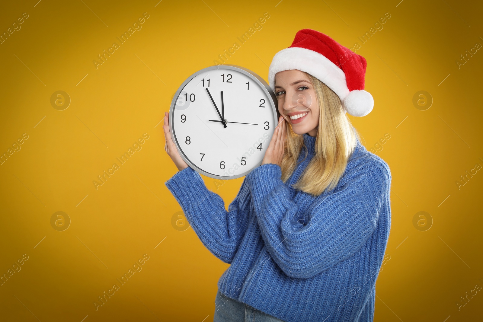 Photo of Woman in Santa hat with clock on yellow background, space for text. New Year countdown