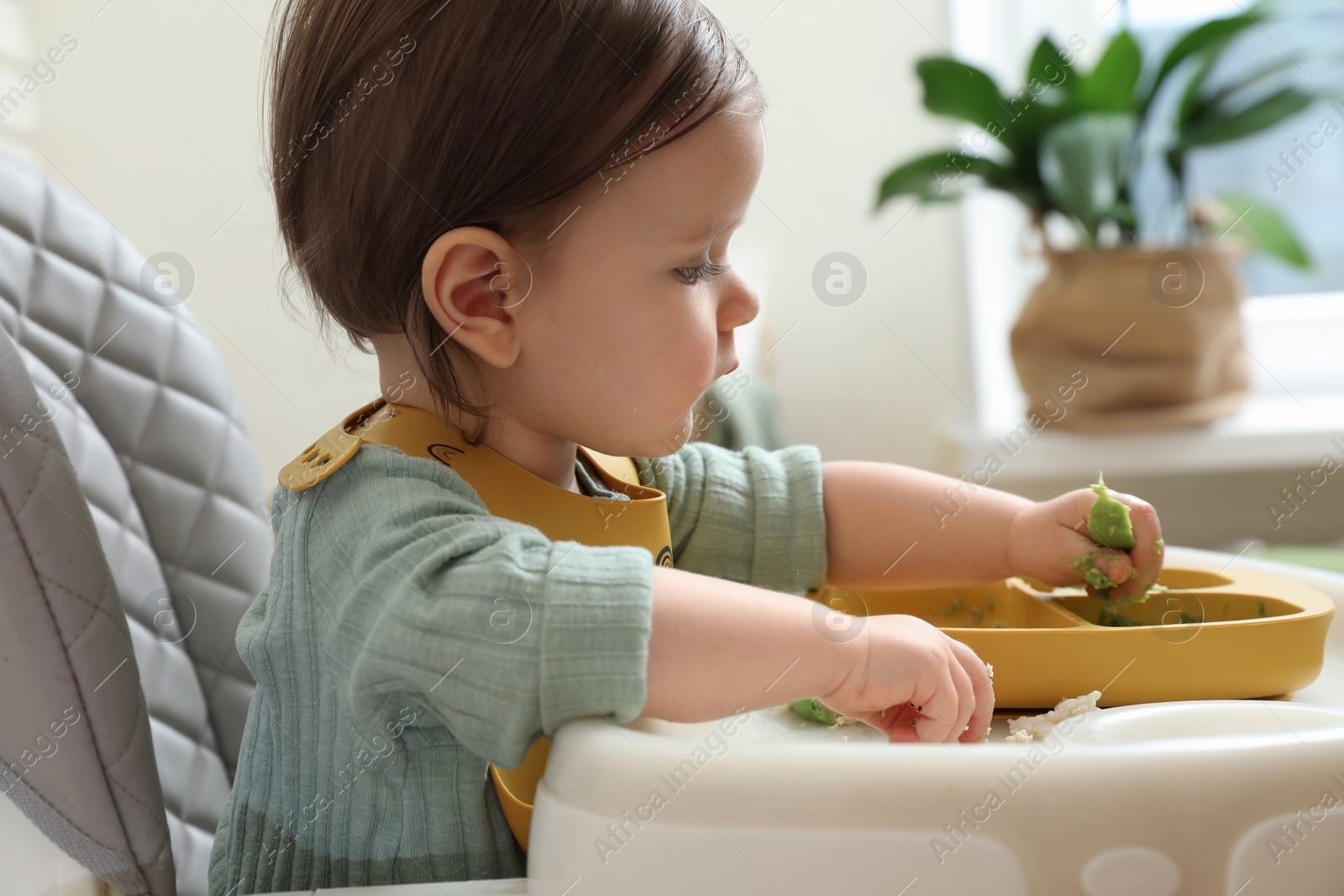 Photo of Cute little baby eating healthy food in high chair indoors