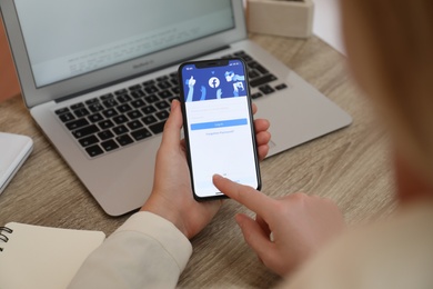 MYKOLAIV, UKRAINE - AUGUST 28, 2020: Woman holding iPhone 11 with Facebook app on screen at table, closeup