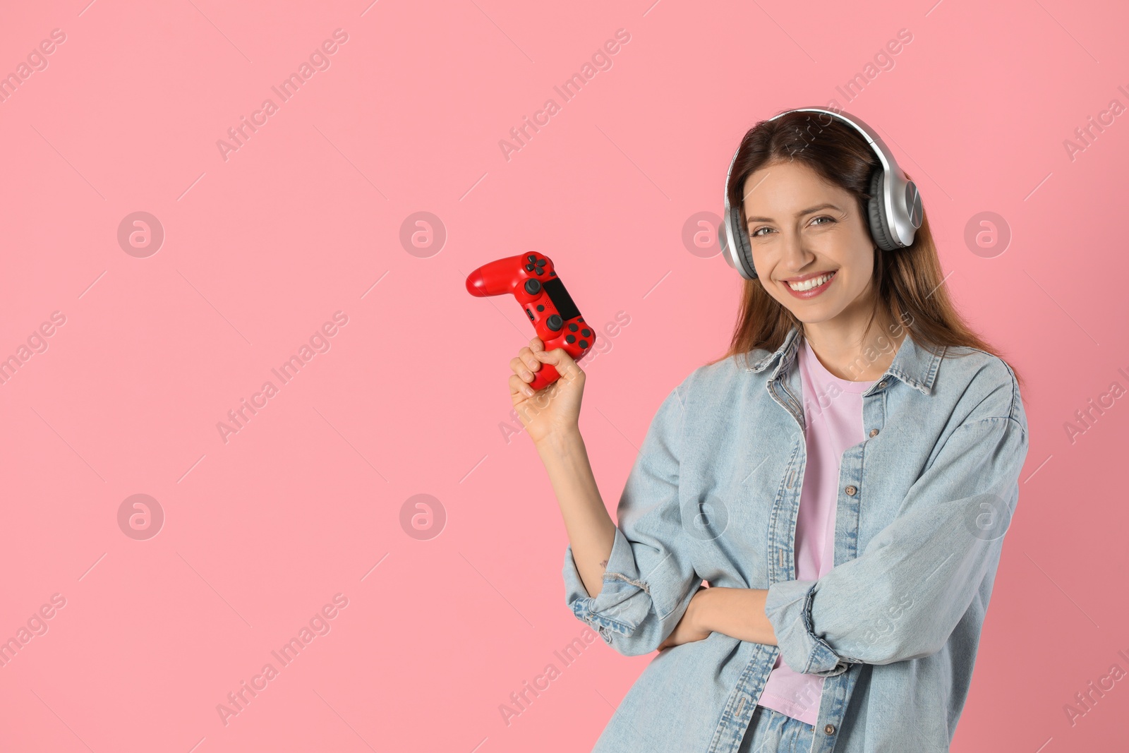 Photo of Happy woman in headphones with game controller on pink background. Space for text