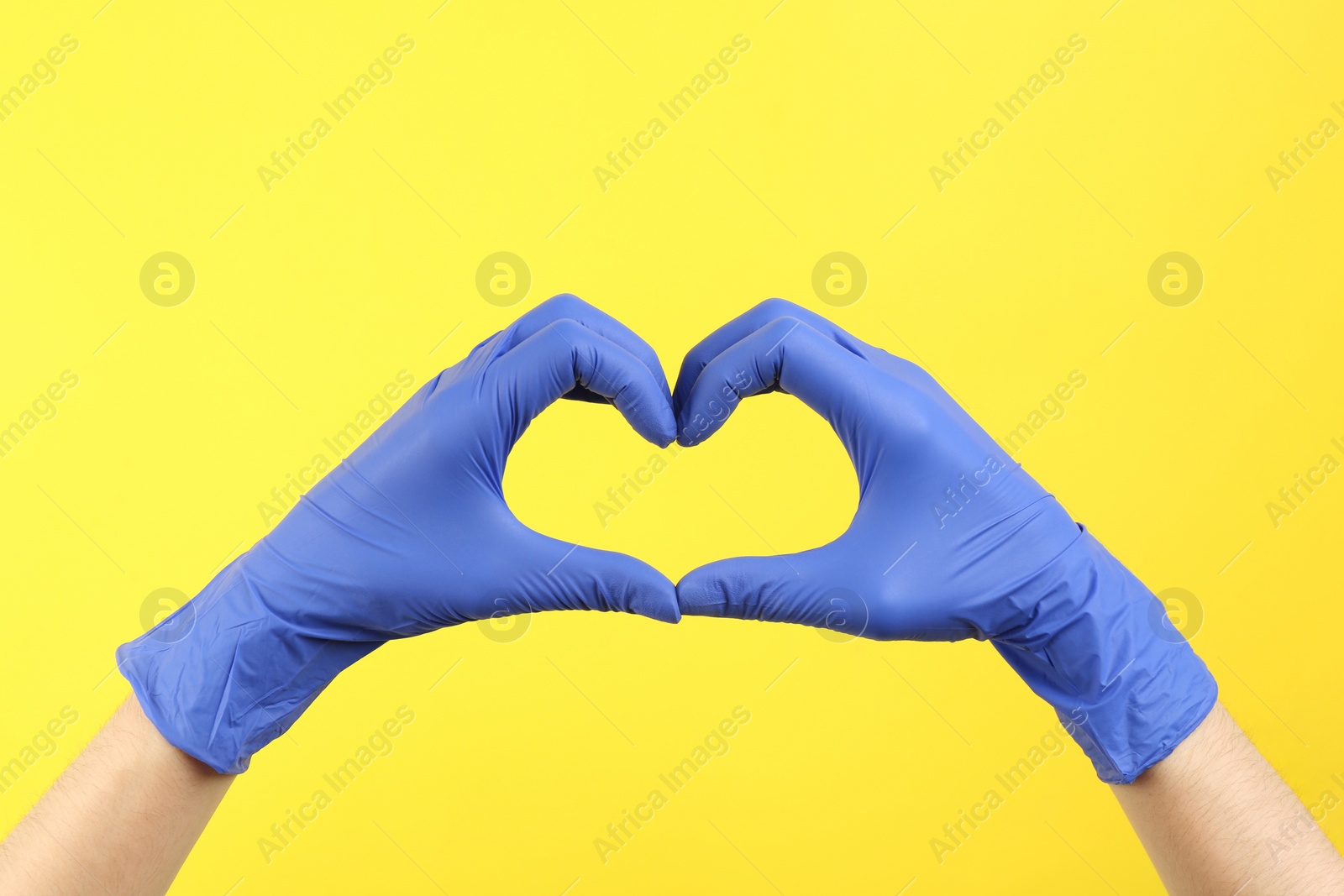 Photo of Person in medical gloves showing heart gesture on yellow background, closeup of hands