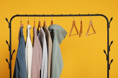 Rack with stylish clothes on wooden hangers against orange background