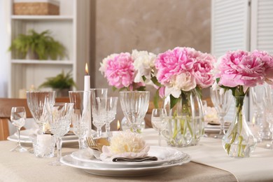 Stylish table setting with beautiful peonies and burning candles indoors