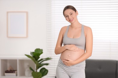 Beautiful pregnant woman standing near sofa at home