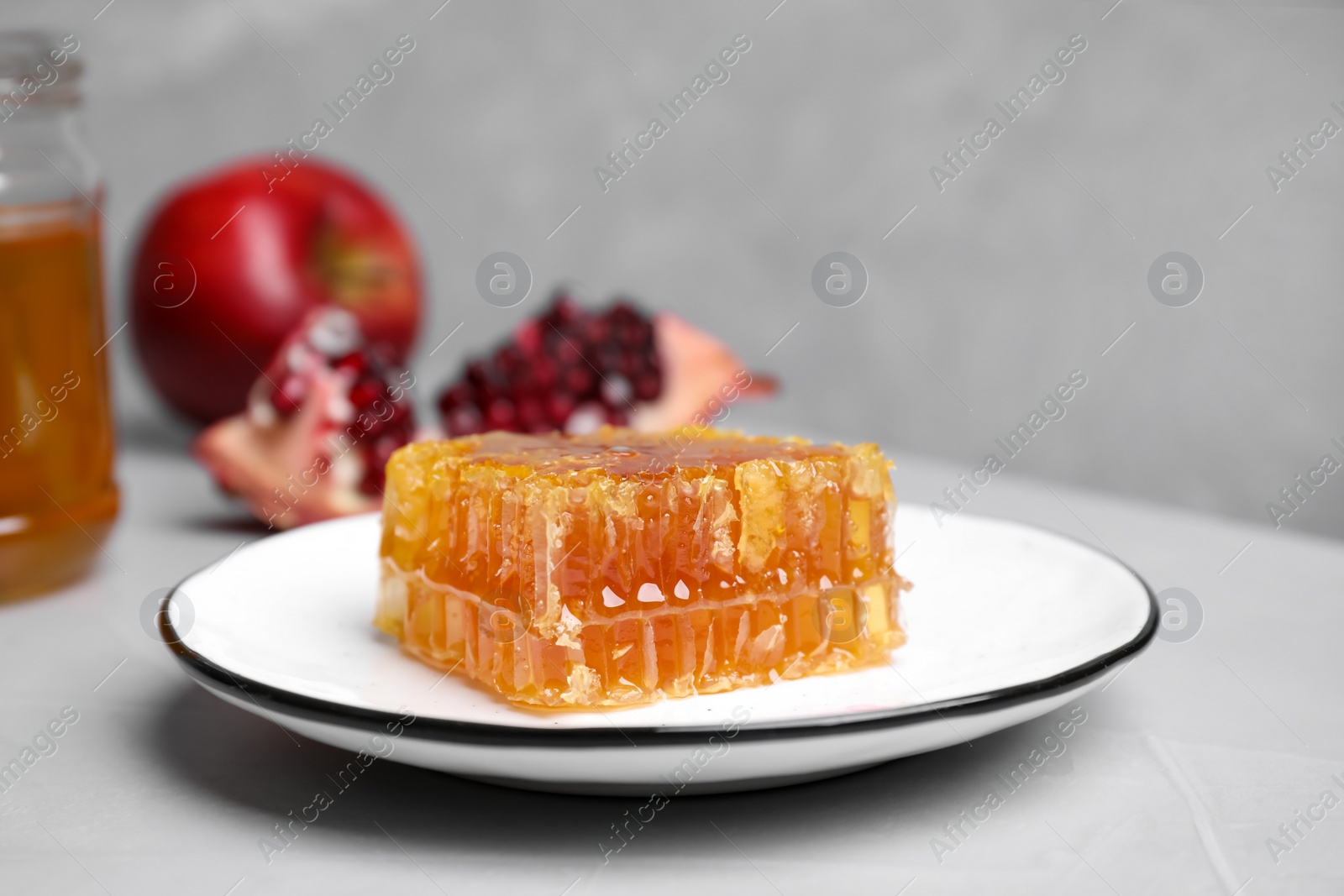 Photo of Honeycomb near pomegranate seeds and apple on light grey table. Rosh Hashanah holiday