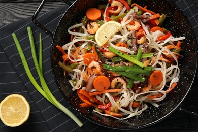 Shrimp stir fry with noodles and vegetables in wok on black wooden table, top view