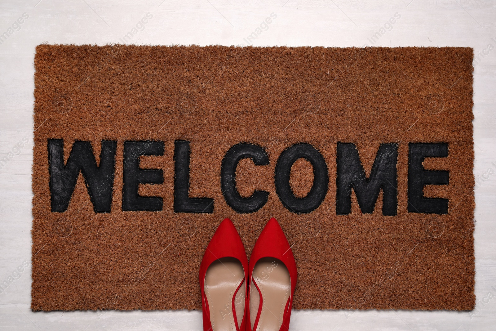 Photo of New clean mat with word WELCOME and shoes on floor, top view