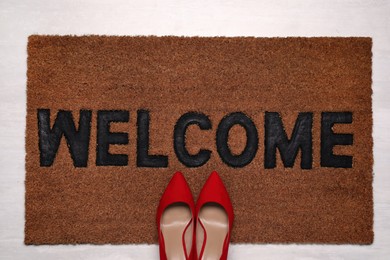 Photo of New clean mat with word WELCOME and shoes on floor, top view