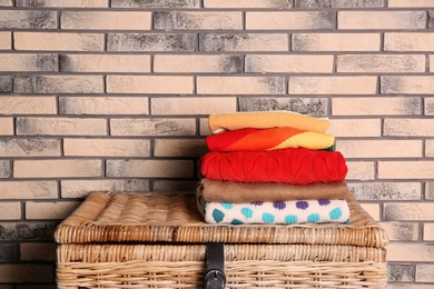 Photo of Stack of colorful winter clothes on wicker chest near brick wall. Space for text