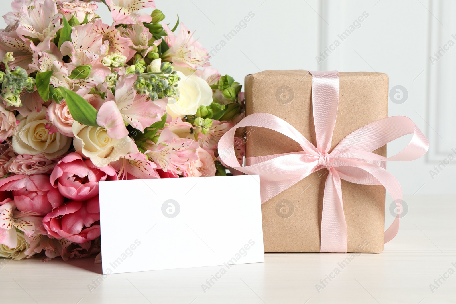 Photo of Happy Mother's Day. Gift box, blank card and bouquet of beautiful flowers on white table. Space for text