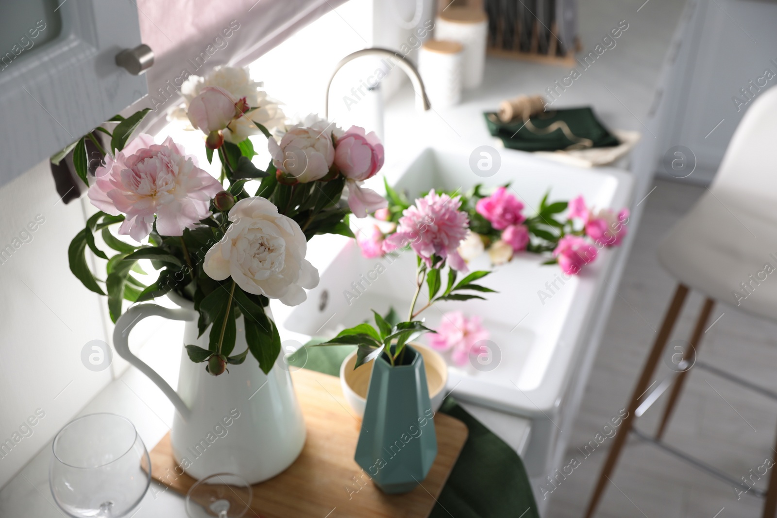 Photo of Beautiful peonies in vases on kitchen counter