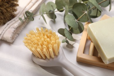 Photo of Cleaning brush, soap bars and eucalyptus leaves on white table, closeup