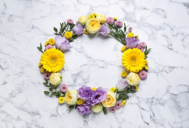 Wreath made of beautiful flowers and green leaves on white marble background, flat lay. Space for text