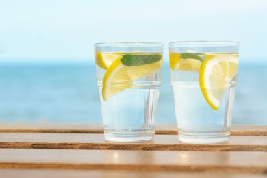 Photo of Refreshing water with lemon and mint on wooden table outdoors, space for text