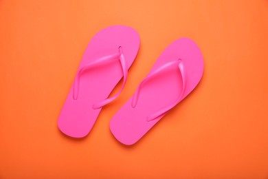 Stylish pink flip flops on orange background, top view