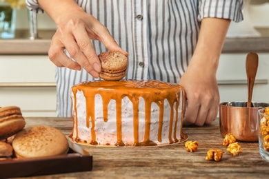 Young woman decorating delicious caramel cake at table