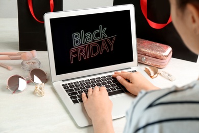 Photo of Woman using laptop with Black Friday announcement at white table, closeup