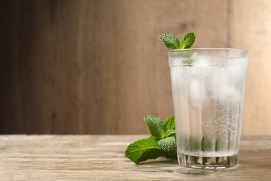 Photo of Glass of soda water with ice and mint on wooden table. Space for text