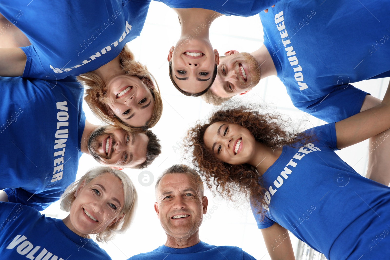 Photo of Team of volunteers joined in circle on light background, bottom view